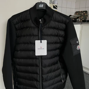 Moncler - Snygg svart Moncler med dragkedja och långärmade ärmar. Perfekt för kyligare dagar.