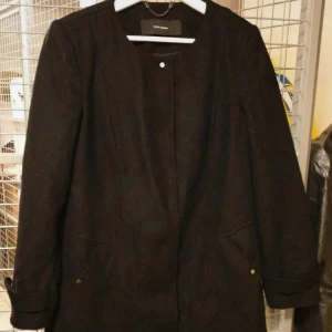 Svart kappa nyskick  - Nyskick Svart kappa med guldfärgade knappar. Kappan har fickor och den är I rak modell. Den har legat nedpackad så rollar av den innan den skickas