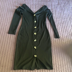 Svart ribbad klänning från Gina Tricot - Säljer en elegant svart ribbad klänning från Gina Tricot. Den har en v-ringad design med knappar hela vägen ner och långa ärmar. Perfekt för både vardag och fest!