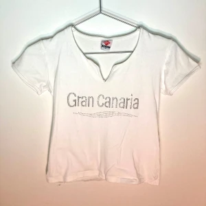 Vit bling magtröja med texten gran canaria - Vit magtröja med texten Gran Canaria skrivet i bling diamanter på, har urigning likt en skjorta  Skulle säga s men även m i storlek beroende på hur tajt