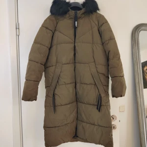 Lång vinterjacka  - En olivgrön lång jacka med faux päls på huvan som är avtagbart. Två större fickor på vardera sida. Från ONLY i storlek XL. Den är i fint skick.
