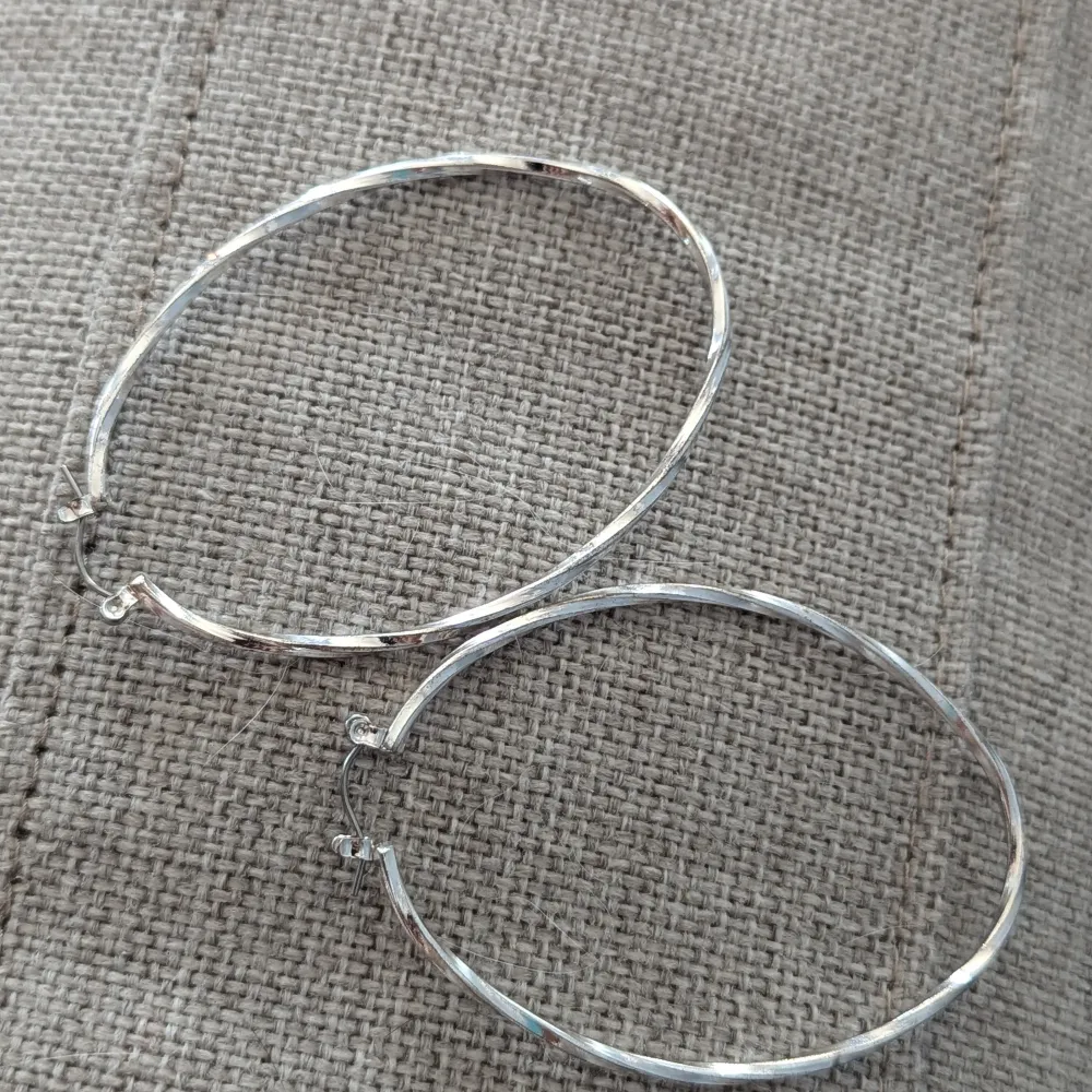 Stora och snygga hoop-örhängen i silverfärg. De är ovala och har en elegant, vriden design som fångar ljuset fint.nyskick. Asusteet.