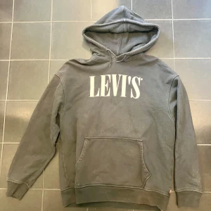 Grå hoodie från Levi's - Säljer en grå hoodie från Levi's i storlek M, oversize. Den är superbekväm och perfekt för både chill och vardag. Har en stor ficka fram och en klassisk luva. Levi's-loggan är tryckt i vitt på bröstet. Perfekt för höst och vinter!