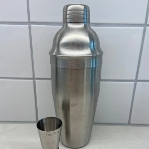 Cocktailskakare och måttkopp 1 oz - Säljer en cocktailskakare med måttkopp (1 oz) och inbyggd sil. Setet är i mycket bra skick och perfekt för hemmabaren.
