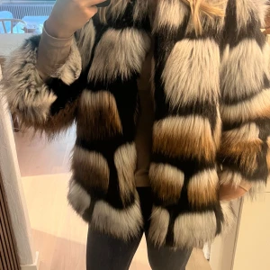 Fuskpälsjacka från Sand - Säljer en supercool fuskpälsjacka från Sand. Den har ett unikt mönster i svart, vitt och brunt som verkligen sticker ut. Jackan är perfekt för höst och vinter och har långa ärmar som håller dig varm. Den är i nyskick och passar perfekt för både vardag och fest!