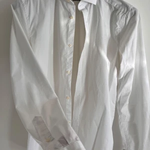 Vit skjorta från Riley - Säljer en stilren vit skjorta från Riley i slim fit. Skjortan är i nyskick och har långa ärmar med knappar. Perfekt för både formella tillfällen och vardagsbruk. Materialet känns skönt och andas bra. Passar perfekt till både jeans och kostymbyxo