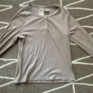 Beige ribbad tröja från H&M - Säljer en snygg och bekväm tröja från H&M. Den har långa ärmar och knappar framtill som ger en stilren look. Perfekt för både vardag och mysiga höstkvällar. Passar till allt!