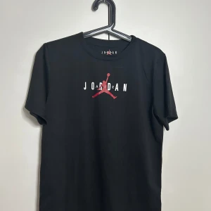 Svart t-shirt från Jordan - Snygg svart t-shirt från Jordan med den ikoniska logotypen på bröstet. Perfekt för en sportig look eller avslappnad stil. Tillverkad i mjukt material för extra komfort. Köpt i USA på en outlet och hittar inte kvittot. Om ni har någon fråga så hör av er! (Priset är inte spikat)