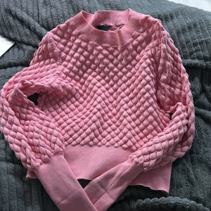 Rosa stickad tröja - Säljer en söt rosa stickad tröja med ett unikt quiltat mönster. Tröjan har långa ärmar och en rund halsringning. Perfekt för kyliga dagar och ger en mysig känsla. Passar bra till både jeans och kjol.