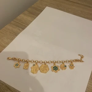 Guldarmband med berlocker - Charmigt guldarmband med flera unika berlocker, inklusive blommor och symboler med turkosa detaljer. Perfekt för att ge en personlig touch till din stil.