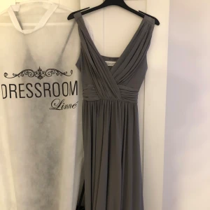 Grå långklänning från Chiara Forthi - Elegant grå långklänning från Chiara Forthi med omlott-design och breda axelband. Klänningen har en v-ringad hals och ett fint fall som ger en stilren look. Perfekt för speciella tillfällen. Klänningen är endast använd 1 gång.