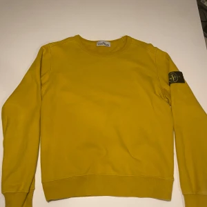 Gul tröja från Stone Island - Säljer en snygg gul tröja från Stone Island med deras ikoniska märke på ärmen. Tröjan har en klassisk rund hals och långa ärmar, perfekt för en stilren look. Skriv ett PM för frågor, bilder etc (priset är ej skrivet i sten) f 