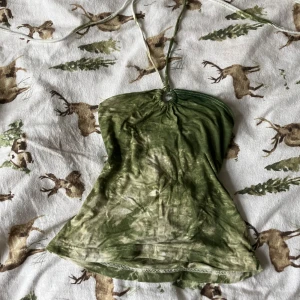 Grön halterneck tubtopp - Säljer en grön halterneck tubtopp med knytband. Toppen har ett unikt batikmönster och är perfekt för sommardagar. Den är tillverkad i ett mjukt och bekvämt material. Den är köpt runt 2003