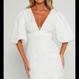 Vit klänning med puffärmar  - Snygg vit kort klänning med puffiga trekvartsärmar och v-ringning. Klänningen har en figurnära passform och ett broderat mönster. Perfekt till studenten. Storlek 38. Använd en gång. Den är från Showpo och slutsåld på hemsidan. 🤍
