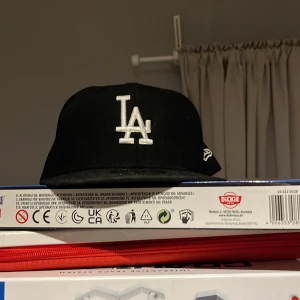 Svart keps från New Era - Snygg svart keps från New Era med LA-logga i vitt framtill. Kepsen är i modellen 59FIFTY och har en platt skärm. Perfekt för en casual look.