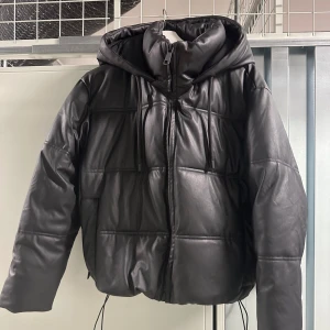 Svart pufferjacka från Zara - Svart pufferjacka från Zara med huva, dragkedja och dragsko i midja. Använd fåtal gånger. 