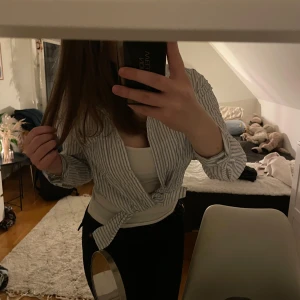 Randig blus med knyt - Säljer en stilren randig blus med knyt framtill. Blusen har långa ärmar och ett klassiskt mönster i vitt och blått. Perfekt för en avslappnad men ändå stilren look.