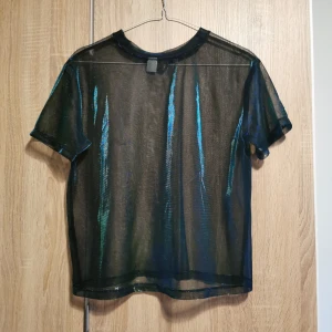 (XS) Grön transparent skimrande topp - Snygg grön transparent topp från H&M med korta ärmar.. Passar bra att bära över ett linne eller en snygg bralette. 