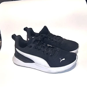 Svarta sneakers från Puma - Snygga svarta sneakers från Puma med vit sula och snörning. Perfekta för en sportig look eller vardagsbruk. De har en stilren design med Pumas logga på sidan.