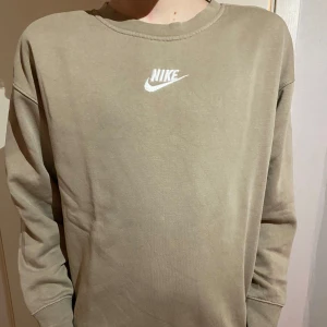 Beige sweatshirt från Nike - Säljer en stilren beige sweatshirt från Nike med deras klassiska logga tryckt på bröstet. Tröjan har en rund halsringning och långa ärmar, perfekt för en avslappnad look. Passar bra till jeans eller träningsbyxor. Skön och enkel att matcha! 🧢