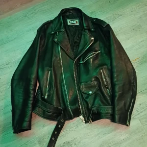 Svart skinnjacka från OSX - Snygg svart skinnjacka från OSX i äkta läder med coola dragkedjedetaljer och bälte i midjan. Jackan har en klassisk bikerstil med långa ärmar och flera fickor. Perfekt för en edgy look!   Nypris:2500kr 