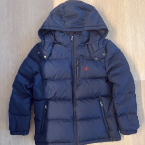 Ralph Lauren Dunjacka - Elegant och tidlös mörkblå dunjacka från Ralph Lauren, perfekt för både vardag och finare tillfällen! Jackan är högkvalitativ samt i fint skick. Hör av er angående minsta fundering, pris är givetvis förhandlingsbart! Observera att jackan är stl 14-16