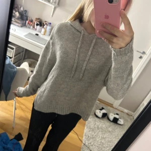 Grå stickad hoodie - Mysig grå stickad hoodie med luva. Perfekt för kyliga dagar med sin avslappnade passform och ribbade muddar vid ärmslut och nederkant. Med små slittar på kanterna. Skriv för mer bilder!
