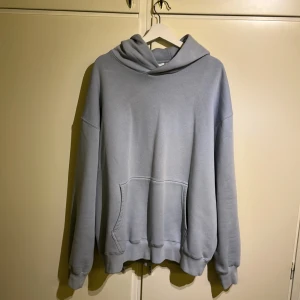 Ljusblå hoodie med tryck - Säljer en ljusblå hoodie med ett coolt tryck på ryggen. Hoodien har en stor ficka framtill och en bekväm passform. Perfekt för en avslappnad stil. Tröjan är storlek XL (loose fit) och sparsamt använd under kortare period innan den blev för stor. Köpt för ca 700kr från Junkyard 