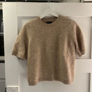 Beige stickad tröja - Säljer en mysig beige stickad tröja med korta ärmar. Perfekt skick! Tröjan har en rund halsringning och ribbade kanter.