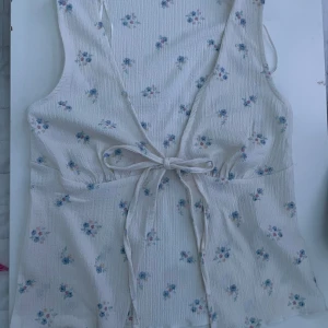Blommigt linne från 157 - Säljer en söt blommig linne från 157 i storlek XS. Linnet är vit med små blommor i blått och rosa och har en knytning framtill. Perfekt för en somrig look!
