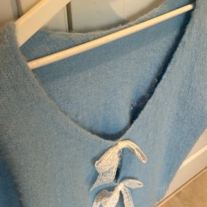 Ljusblå stickad tröja med rosetter - Charmig ljusblå stickad tröja med korta ärmar och v-ringning. Tröjan har fina vita rosetter framtill som ger en söt detalj. Kan användas på båda sidorna. Köpt på mitt tidigare jobb, därav ingen märkning och one size. Men otroligt fin o unik!!