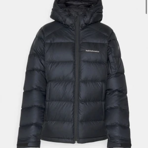 Svart dunjacka från Peak Performance - Snygg och varm svart dunjacka från Peak Performance med huva och dragkedja framtill. Perfekt för kyliga dagar med sin pufferdesign som håller värmen | den har ett mini hål på armen som inte syns därav priset och två fickor går ej att stänga | kp för egna bilder pris är inte fastspikat | nypris 4k