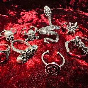 Set med nio matchande ringar med dödskallar rosor och ormmotiv - Säljer ett set av nio coola silverfärgade ringar med olika motiv, inklusive dödskallar, en orm och två rosor. Perfekt för att ge din stil en edgy touch. Ringarna har detaljerade mönster och är justerbara för att passa olika fingrar.