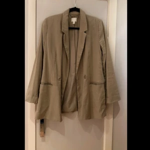 Beige kavaj från H&M - Snygg beige kavaj från H&M i storlek S. Tillverkad av en blandning av viskos och polyester, vilket ger en skön och lätt känsla. Kavajen har en klassisk design med knappar framtill och långa ärmar. Perfekt för en stilren look.                     Längd: 79 cm  Ärm: 44 cm Bredd/byst (runt): 92 cm                             Mintgrön (går lite mot grått)