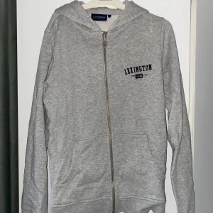 Grå hoodie från Lexington - Säljer en stilren grå hoodie från Lexington med dragkedja och huva. Däremot saknas snörerna