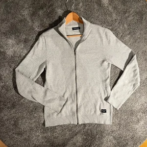 Grå kofta från Jack & Jones - Snygg och stilren grå kofta från Jack & Jones med dragkedja. Den är i väldigt bra skick och har inga defekter. Hör av er vid funderingar