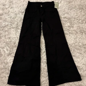 Svarta vida byxor från H&M - Snygga svarta byxor från H&M med vida ben och hög midja. Byxorna har fickor fram och en knappstängning. Perfekta för en trendig look.