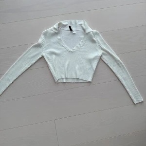 Vit ribbad croppad tröja - Snygg vit ribbad tröja med croppad passform och v-ringad hals. Perfekt för en stilren look. Långärmad design som passar bra till både jeans och kjol.