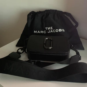 Svart axelväska från Marc Jacobs - Snygg svart axelväska från Marc Jacobs med en bred axelrem och logotypdetalj. Väskan har en dragkedja och en stilren design. Dustbag tillkommer. Helt oanvänd.
