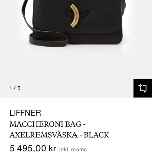 Svart axelremsväska från Little Liffner - Elegant svart axelremsväska från Little Liffner med en unik gulddetalj på framsidan. Väskan har en stilren design och justerbar axelrem, perfekt för en chic look. Helt ny, aldrig använd