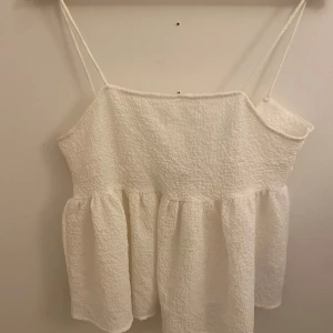 Vit linnetopp från ONLY - Aldrig andvänd. Säljer en söt vit linnetopp från ONLY med smala axelband och en fin knytdetalj i ryggen. Toppen har en luftig och avslappnad passform, perfekt för varma sommardagar.