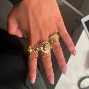 Guld ringar  - Säljer dessa tre guldringar. Den i mitten är från Gina tricot och de andra är från egenföretag. Den från Gina är storlek s, den med en rosett är justerbar och den med ett hjärta är i storlek 7. En kostar 50. Två kostar 90. Tre kostar 130. Fint skick, nästintill oanvända🥰