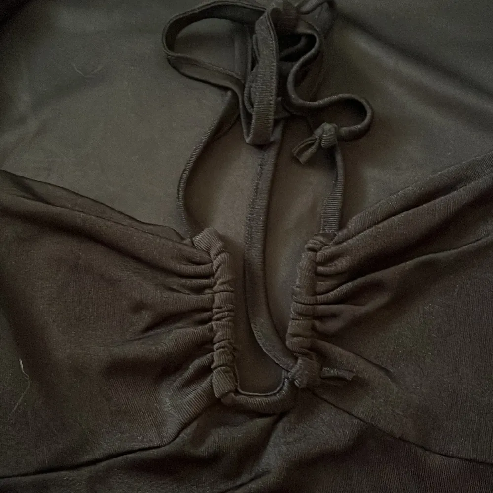 Snygg svart klänning med lång ärm och knytning framtill. Perfekt för en stilren look med en touch av elegans. Klänningen har en åtsittande passform som framhäver figuren.. Mekot.