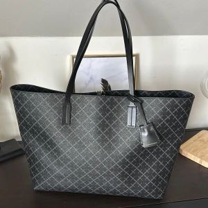 Svart och grå shoppingväska med rutigt mönster - Snygg shoppingväska i svart och grått med ett stilrent rutigt mönster. Väskan har svarta handtag och en praktisk dragkedja på insidan. Perfekt för att bära med sig allt man behöver under dagen.