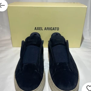 Svarta sneakers från Axel Arigato - Snygga svarta sneakers från Axel Arigato i mocka med en stilren design. Skorna har en vit sula som ger en fräsch kontrast. Perfekta för en avslappnad och trendig look. Storlek 40 men passar även upp till 42. (Stor i storleken)