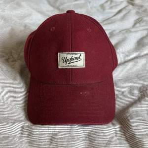 Vinröd keps från Upfront - Snygg vinröd keps från Upfront med justerbar rem baktill. Kepsen har en broderad logotyp framtill och är perfekt för en avslappnad stil.