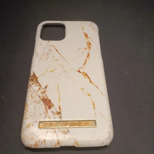 Iphone 11 pro mobilskal från iDeal of Sweden - Snyggt mobilskal med marmormönster i vitt och guld från iDeal of Sweden. Skalet har en elegant design med en metallisk logotypdetalj. Perfekt för att ge din telefon ett stilrent utseende.