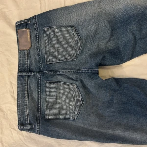 DKNY jeans med låg midja och flared modell - DKNY jeans med en låg midja och flared modell, storlek 26 i jättebra skick. Rhinestones på bakfickorna. midja: 36cm, grenmått: 20cm, innerbenslängd: 84cm, benöppning: 24 cm.