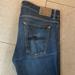 Blå jeans från Nudie Jeans - Snygga blå jeans från Nudie Jeans med klassisk femficksdesign och orange sömmar. Storlek 34/34 och är i bra skick! Nypris är runt 1500 kr på dessa så jag säljer för endast 549