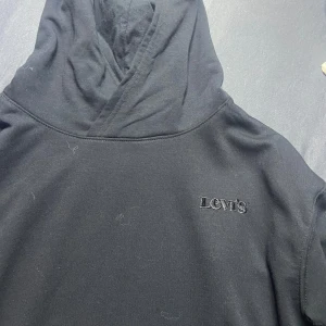 Svart hoodie från Levi's - Säljer en stilren svart hoodie från Levi's med broderad logga på bröstet. . Hoodien har en klassisk design med huva och är tillverkad i ett mjukt material.